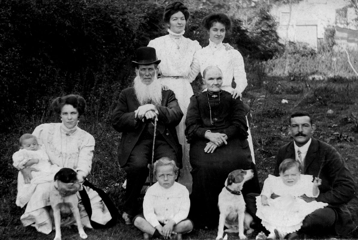 a family group with two old people, three young women, a man, three children and two dogs