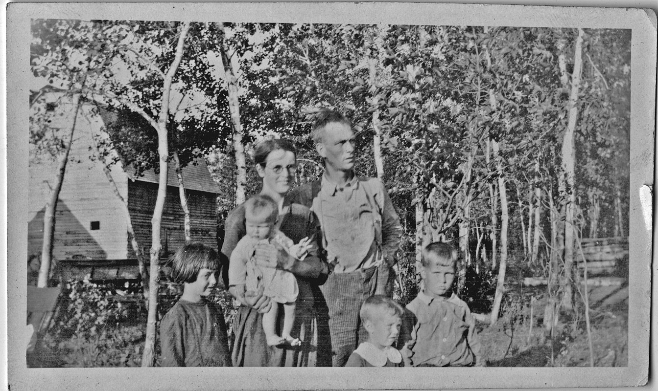old photograph of family standing in forest beside wooden barn